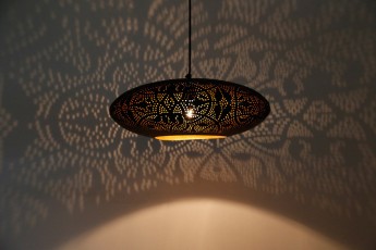 filigrain zwart goud hanglamp met dezelfde patronen en reflectie's op muur